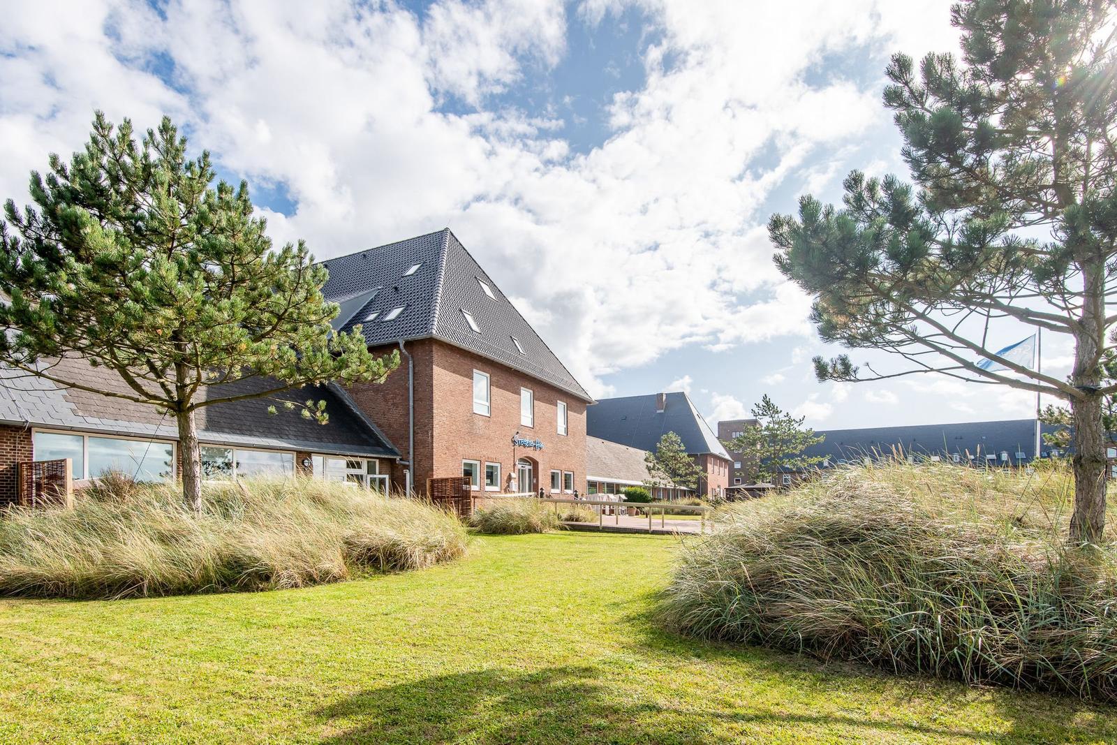 Ein modernes, zweistöckiges Gebäude mit Garten und Bäumen unter einem bewölkten Himmel.
