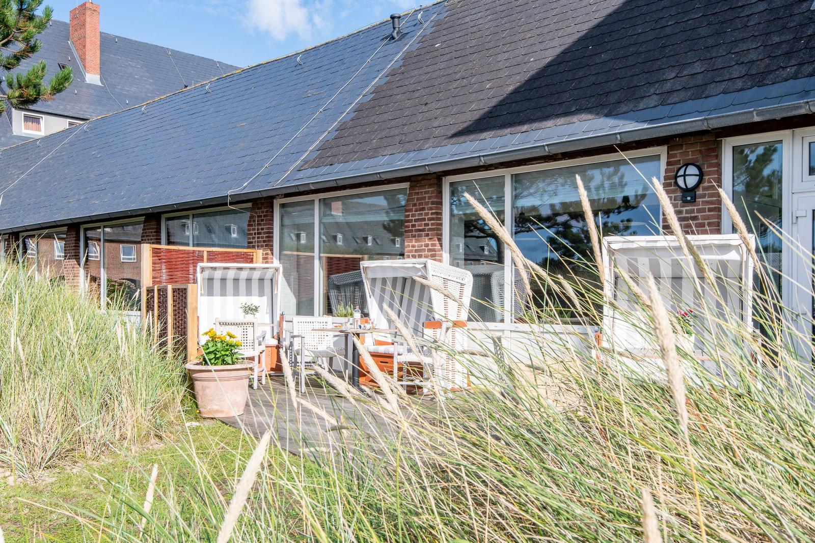 Terrasse mit Liegestühlen und Pflanzen vor einem Haus mit großen Fenstern.
