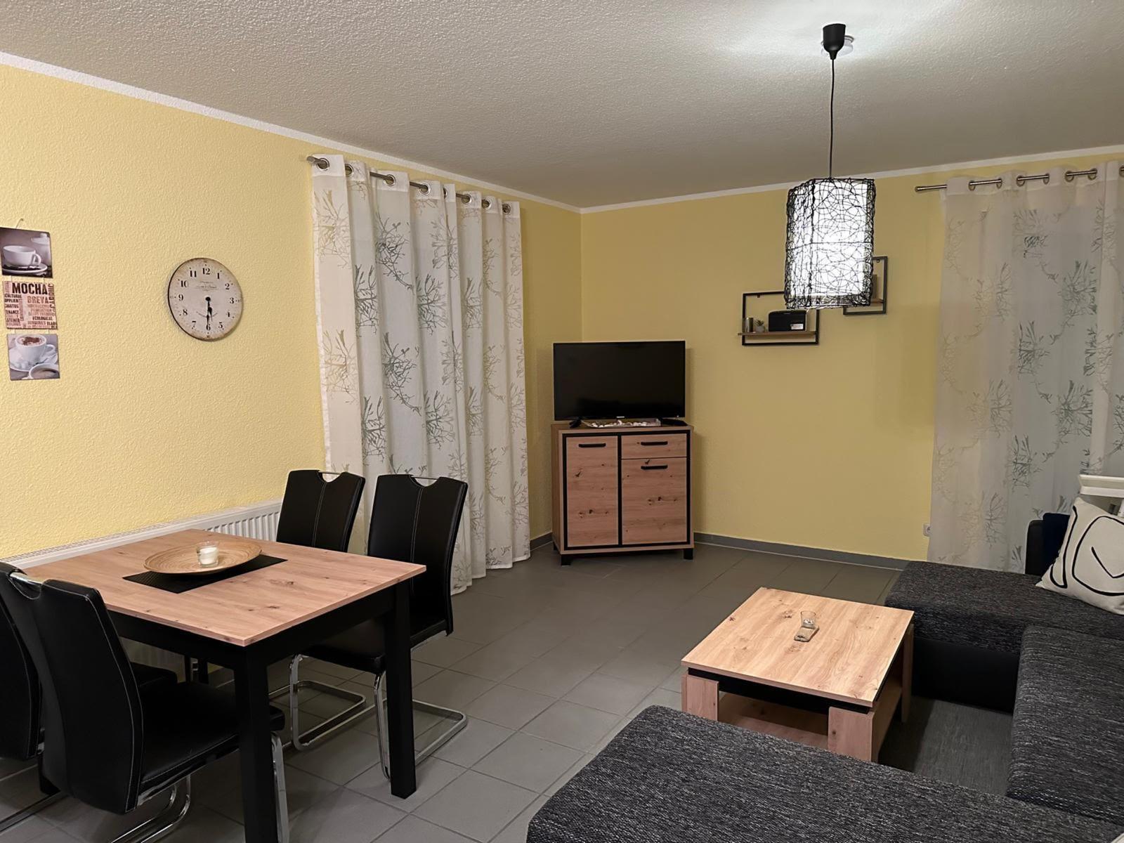 Wohn- und Essbereich mit Sofa, Esstisch, TV und Vorhängen.
