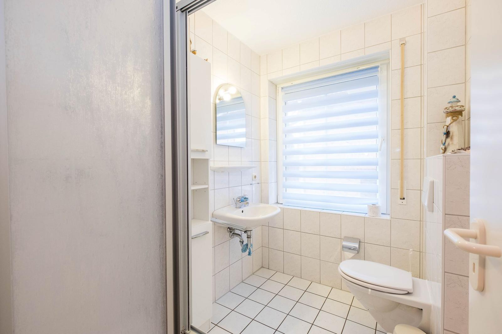 Badezimmer mit Toilette, Waschbecken und Fenster mit Jalousie.