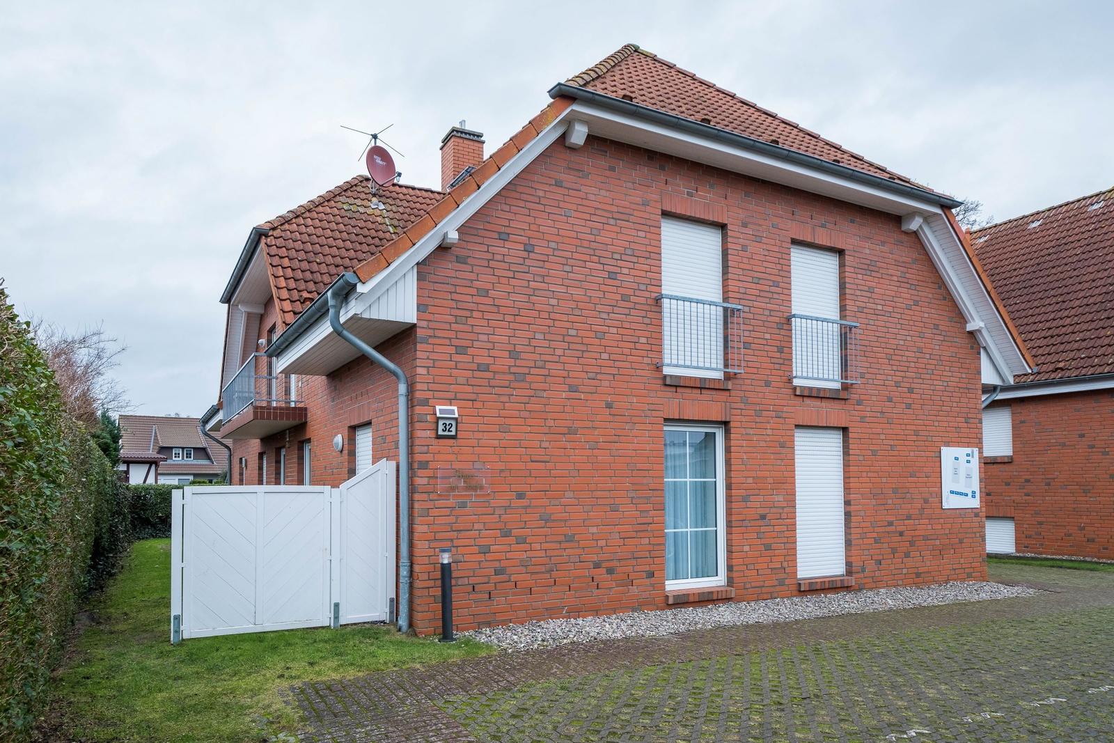 Rotes Backsteinhaus mit weißen Fensterläden und Balkon. Weiße Toranlage und gepflasterter Hof.