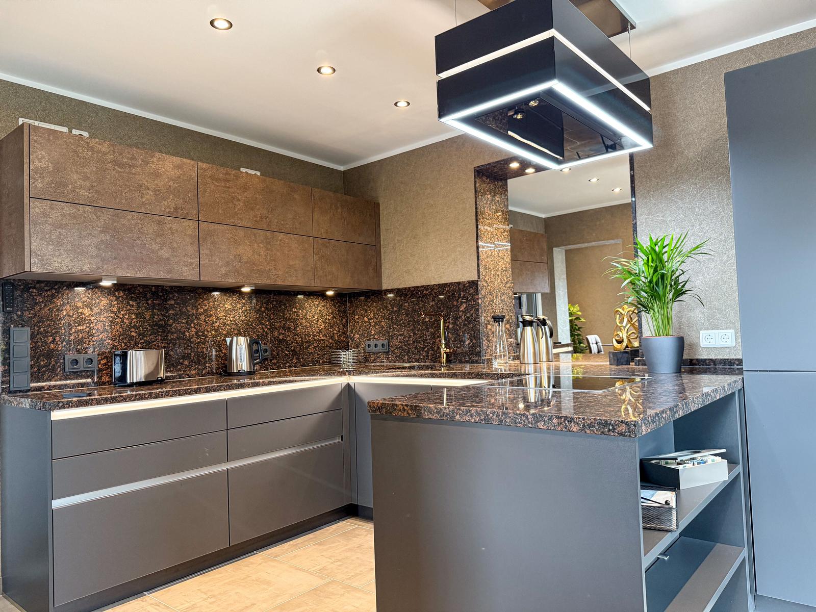 Moderne Küche mit dunklen Schränken, Marmorarbeitsplatte und moderner Beleuchtung.