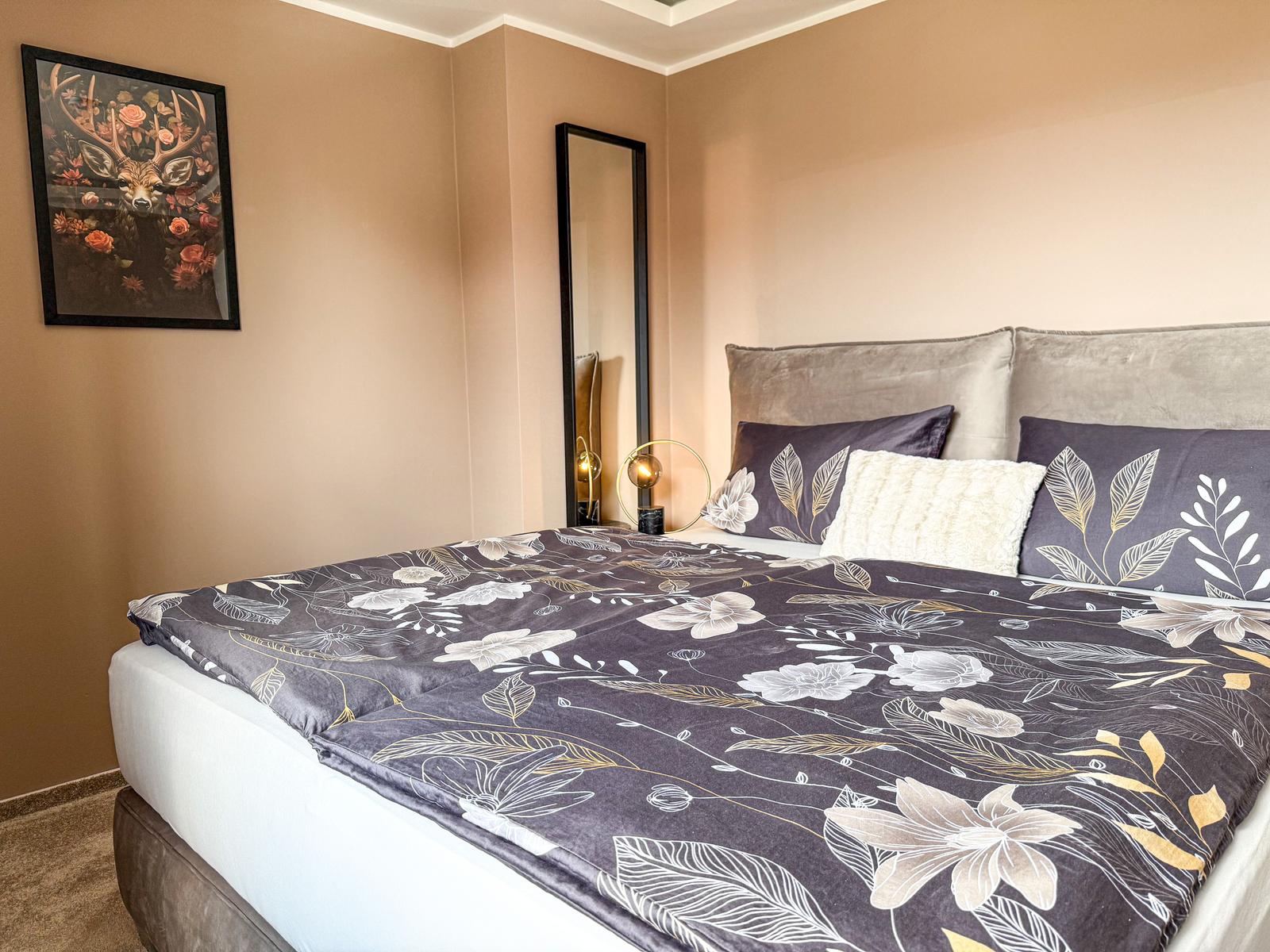 Schlafzimmer mit Bett, Wandspiegel und Wandbild mit Hirschmotiv.