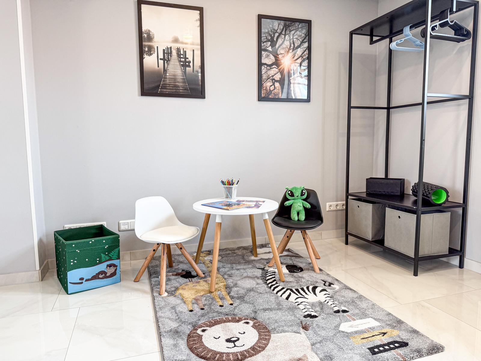 Kinderzimmer mit Tisch, Stühlen, Teppich und Kleiderständer.