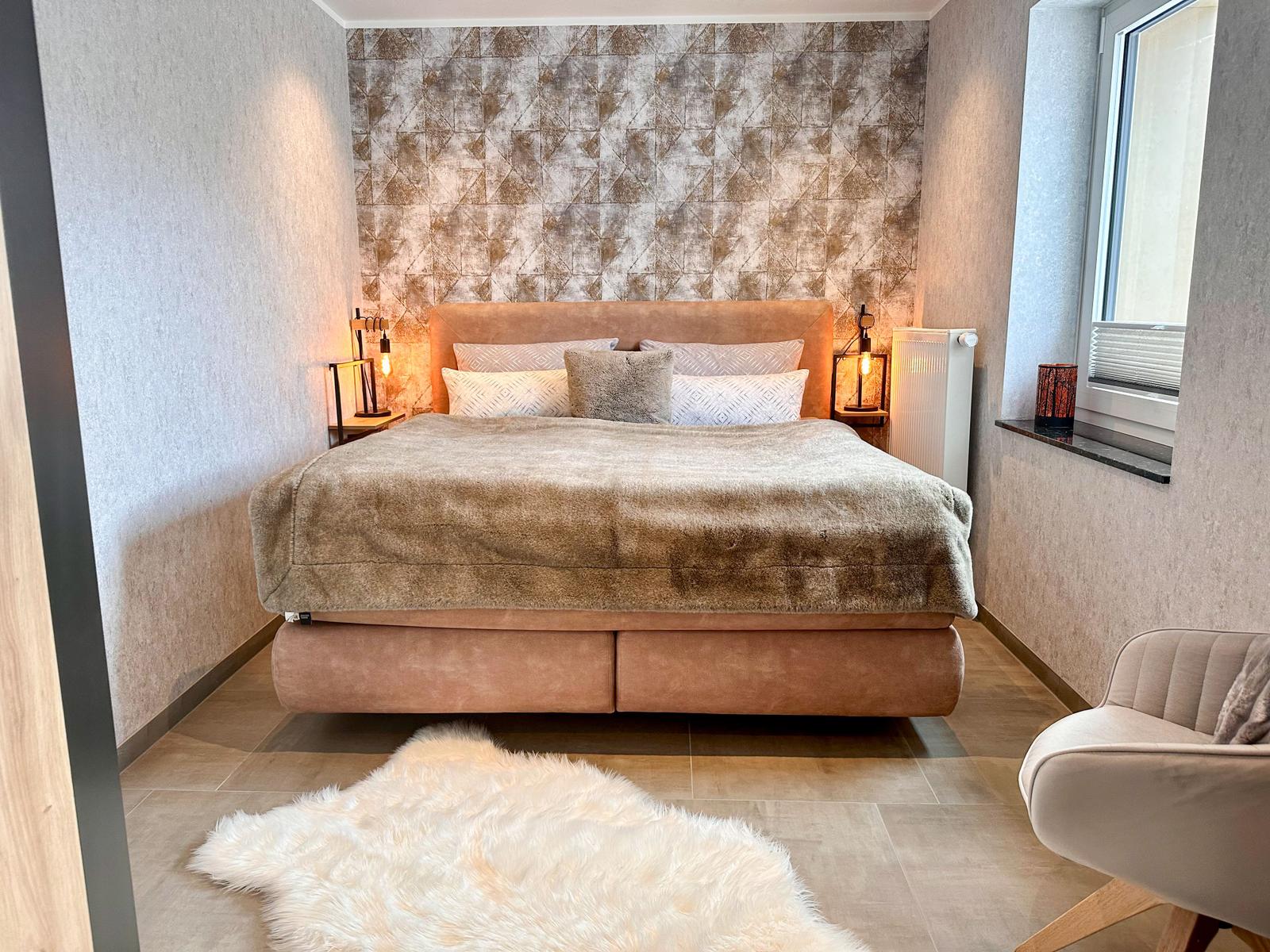 Schlafzimmer mit Bett, Wandbeleuchtung und Sitzgelegenheit.