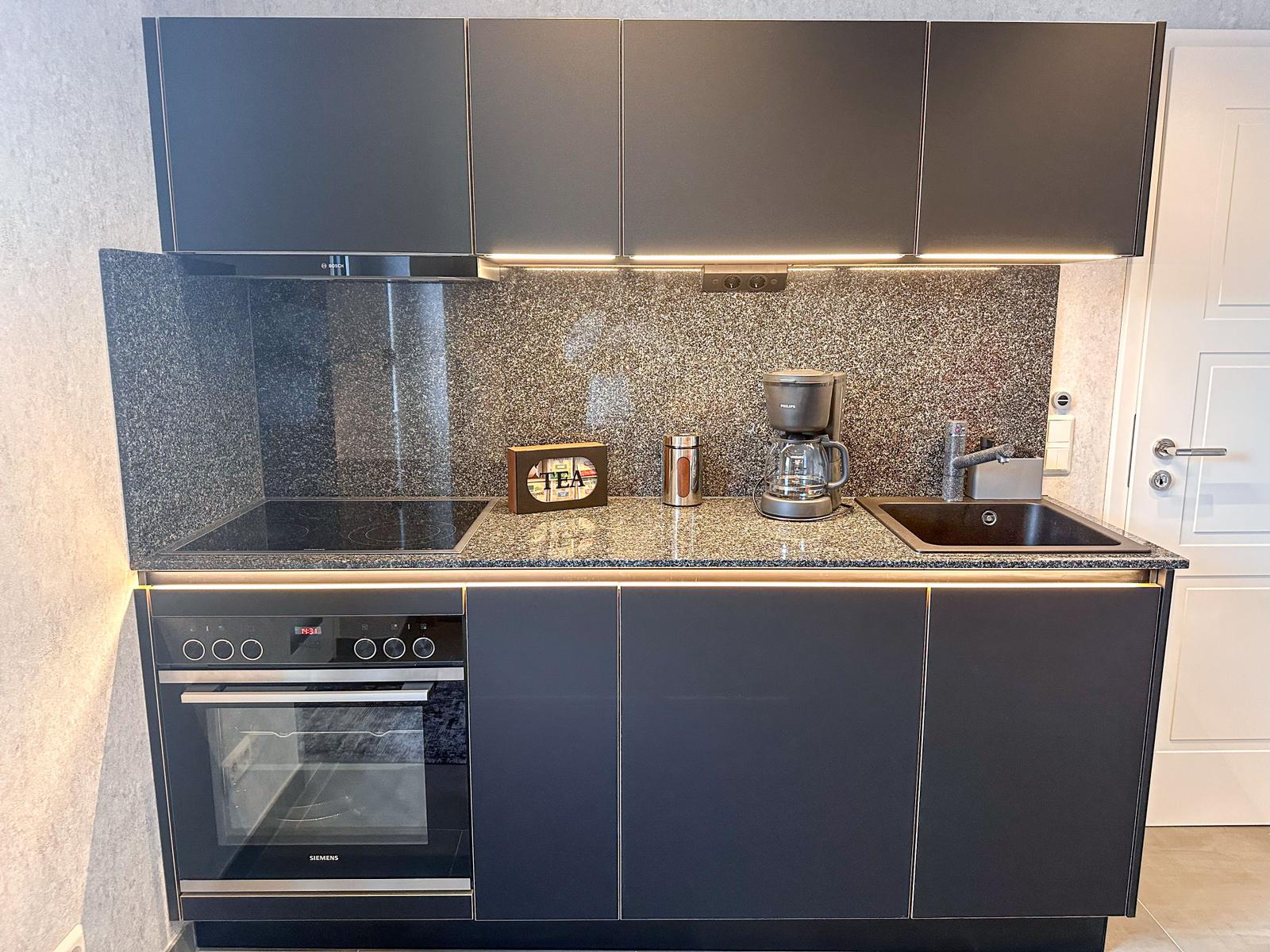 Küche mit Dunstabzug, Herd, Backofen und Spüle.