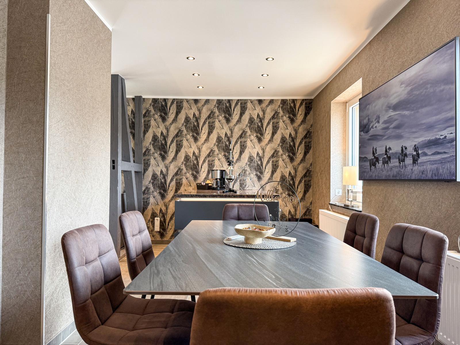 Esszimmer mit Tisch, Stühlen und Wandbild. Hintergrundwand mit Muster.