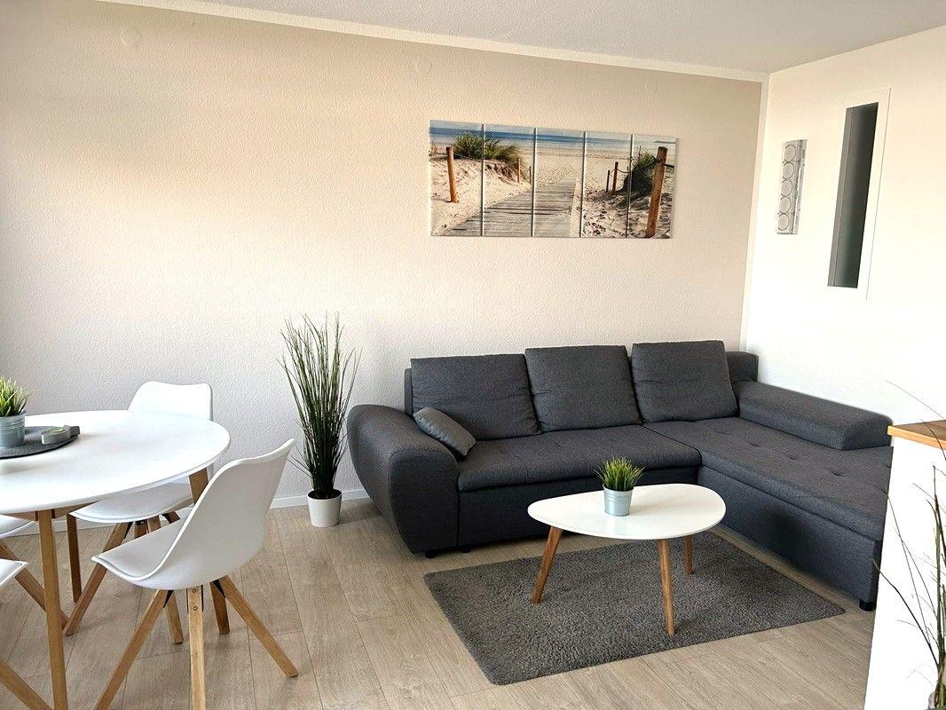Wohn- und Essbereich mit grauem Sofa, runden Tischen und Wandbildern.
