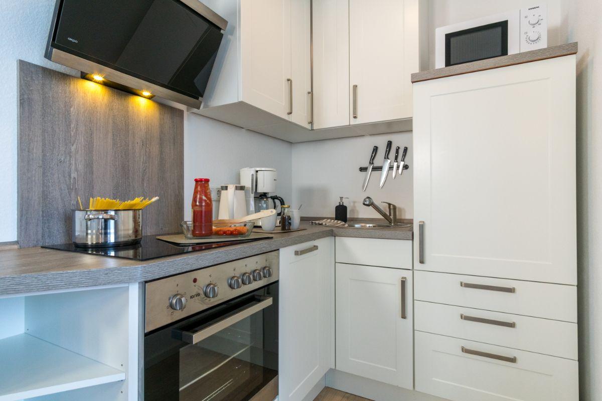 Küche mit weißen Schränken, Herd, Dunstabzug und Spüle.