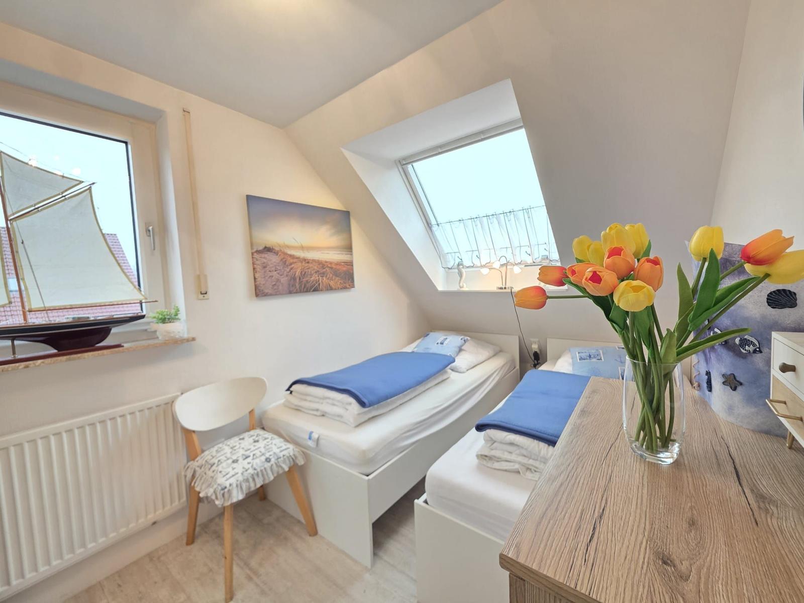 Room with two single beds, skylight, and window with sailboat model.