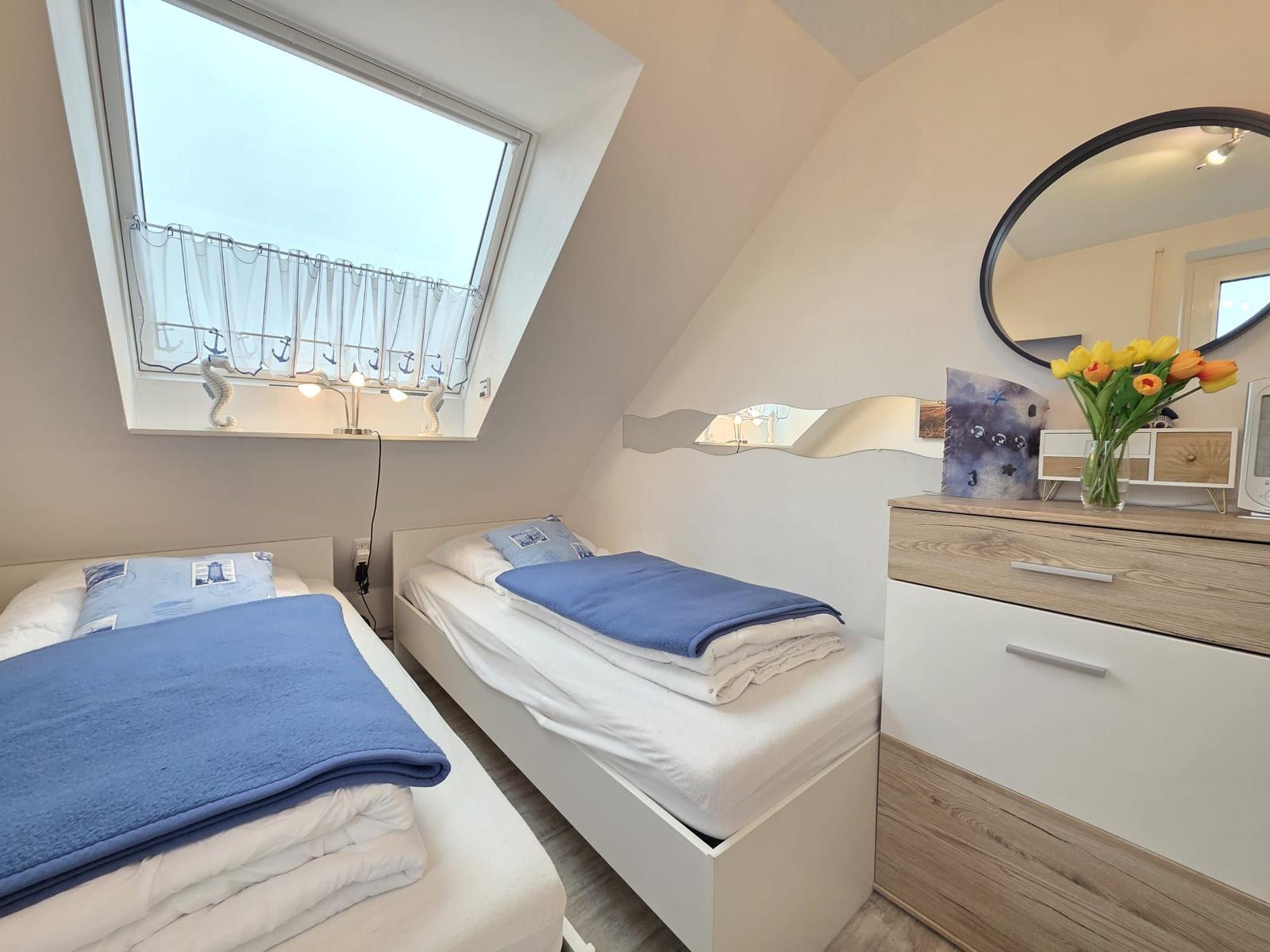 Two single beds under sloped ceilings with window and makeup table.