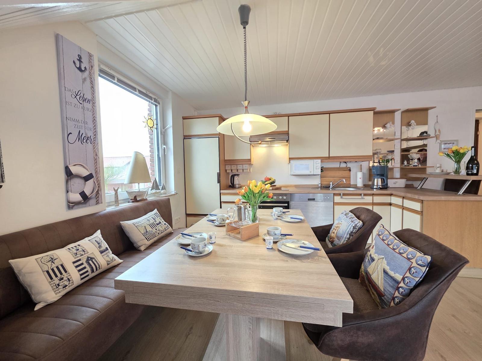 Dining area with kitchenette and window. Wooden table, chairs, cushions, and decor.