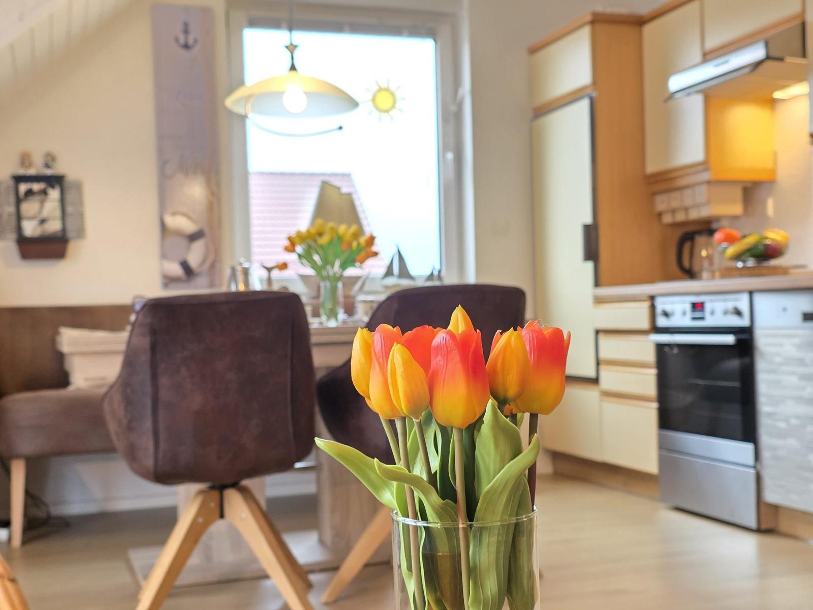 Kitchen and dining area with tulips, chairs, and window view.