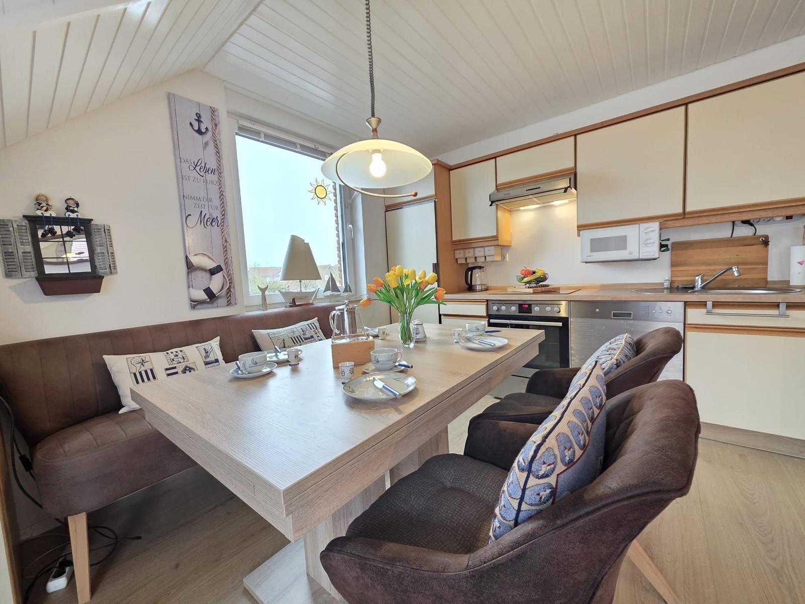 Dining area with table, bench, and kitchen. Window with sea motif.