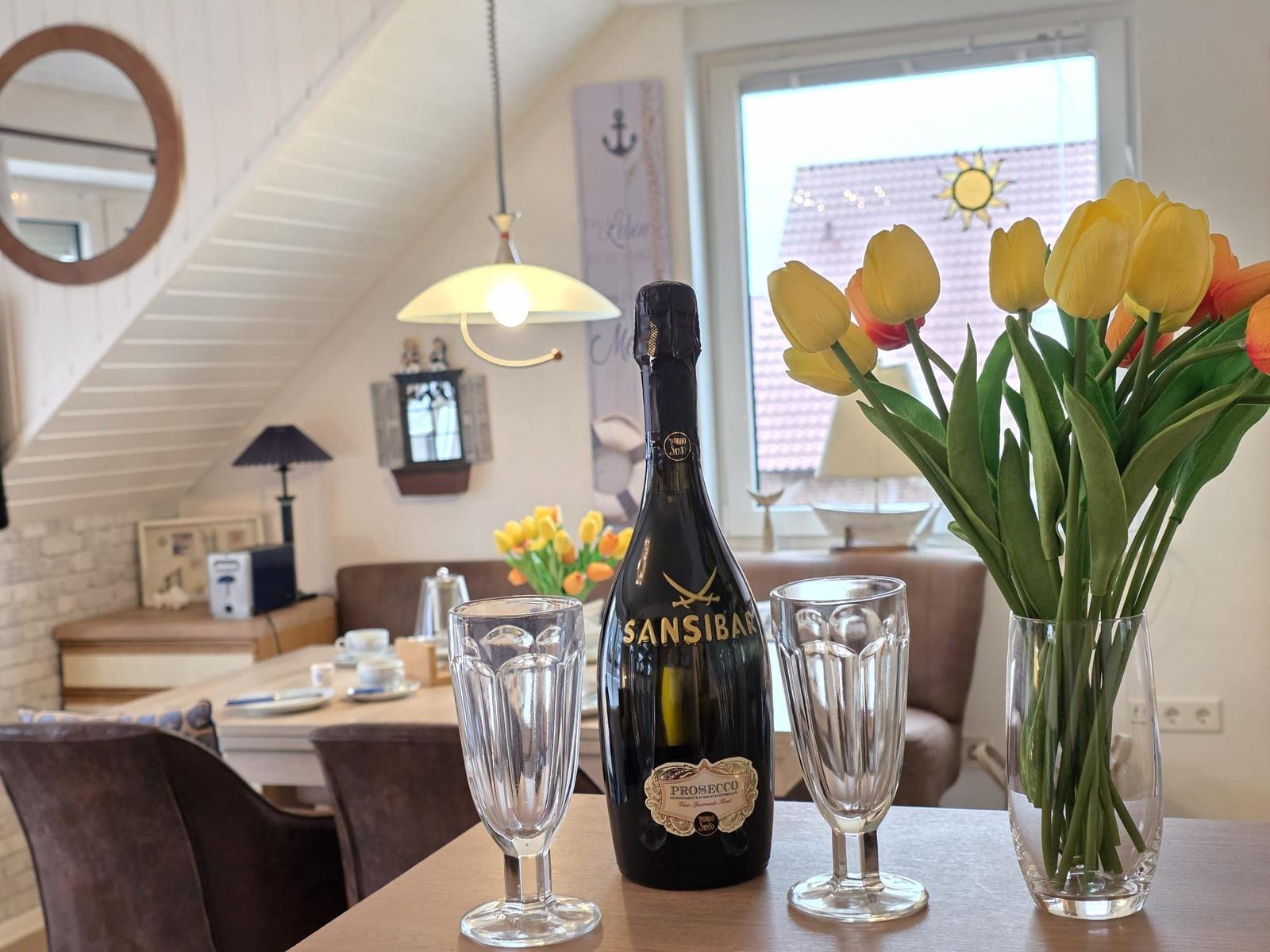 Table with flowers, prosecco, and glasses in dining room with window and beams.
