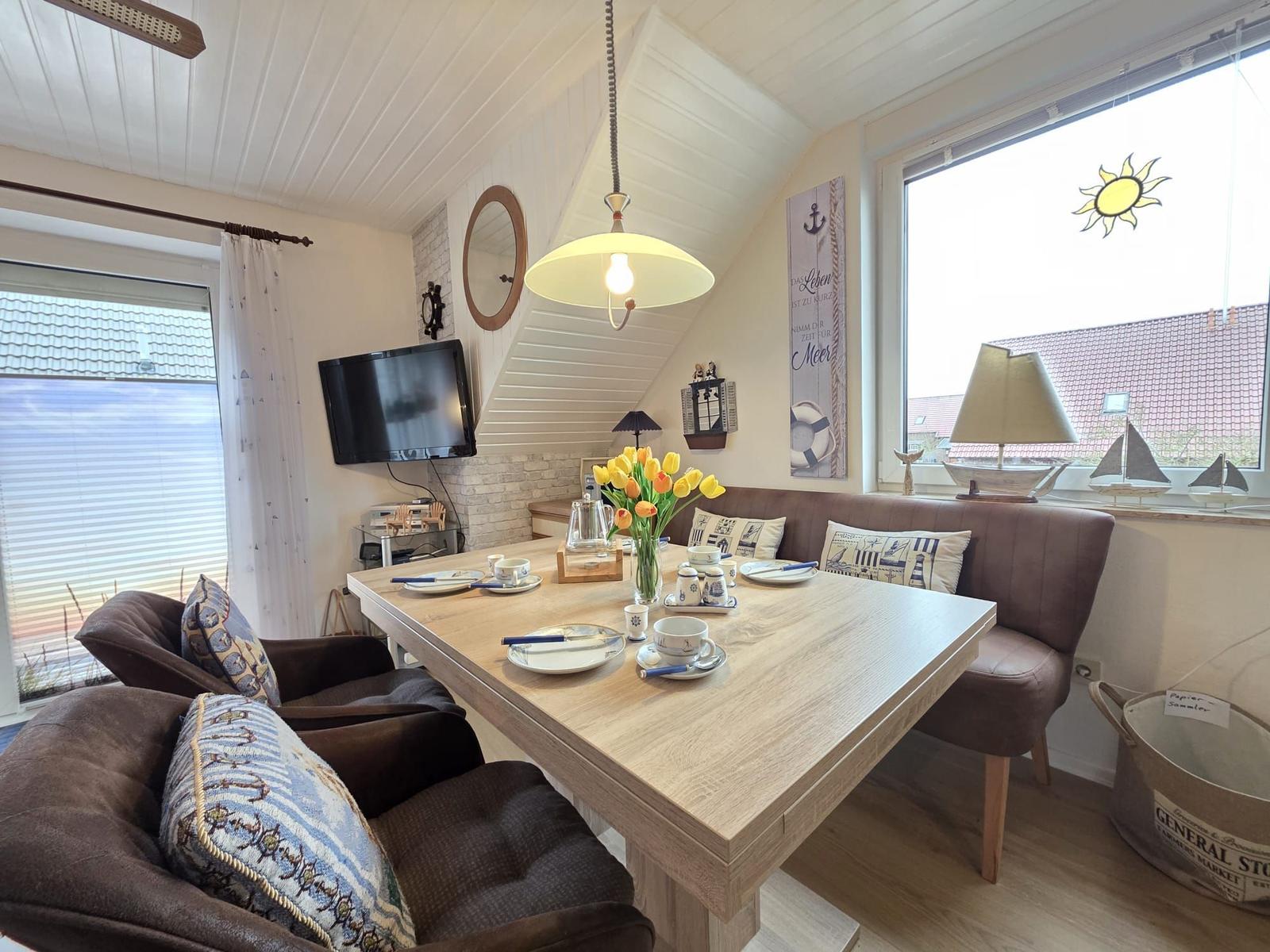 Dining room with wooden table, bench, and windows. Decorated with flowers and sailboats.