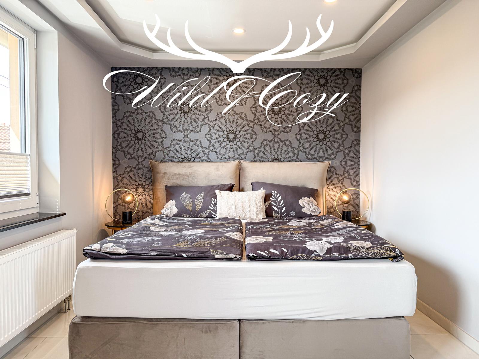 Schlafzimmer mit Doppelbett, gemusterter Wand und Nachttischen mit Lampen.