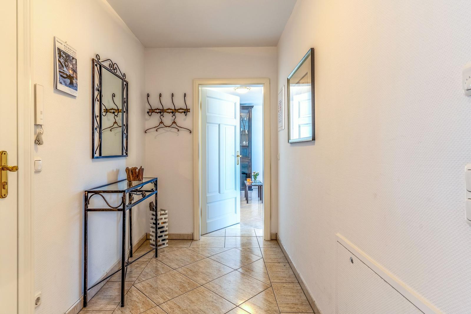 Flur mit Spiegel, Garderobe und Tisch. Tür führt in Wohnbereich.