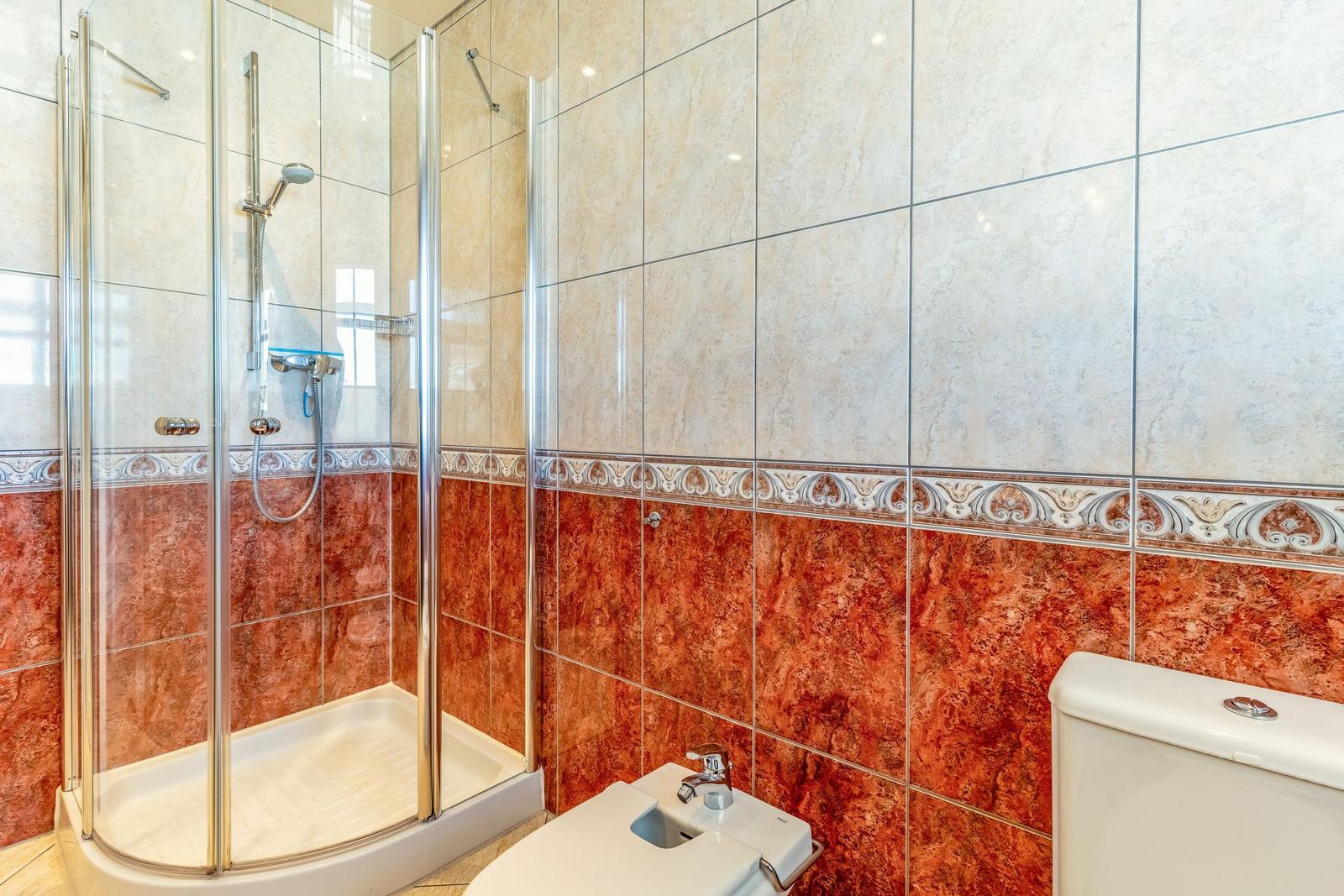 Bad mit Dusche, Toilette und Fliesen in Rot- und Beigetönen.