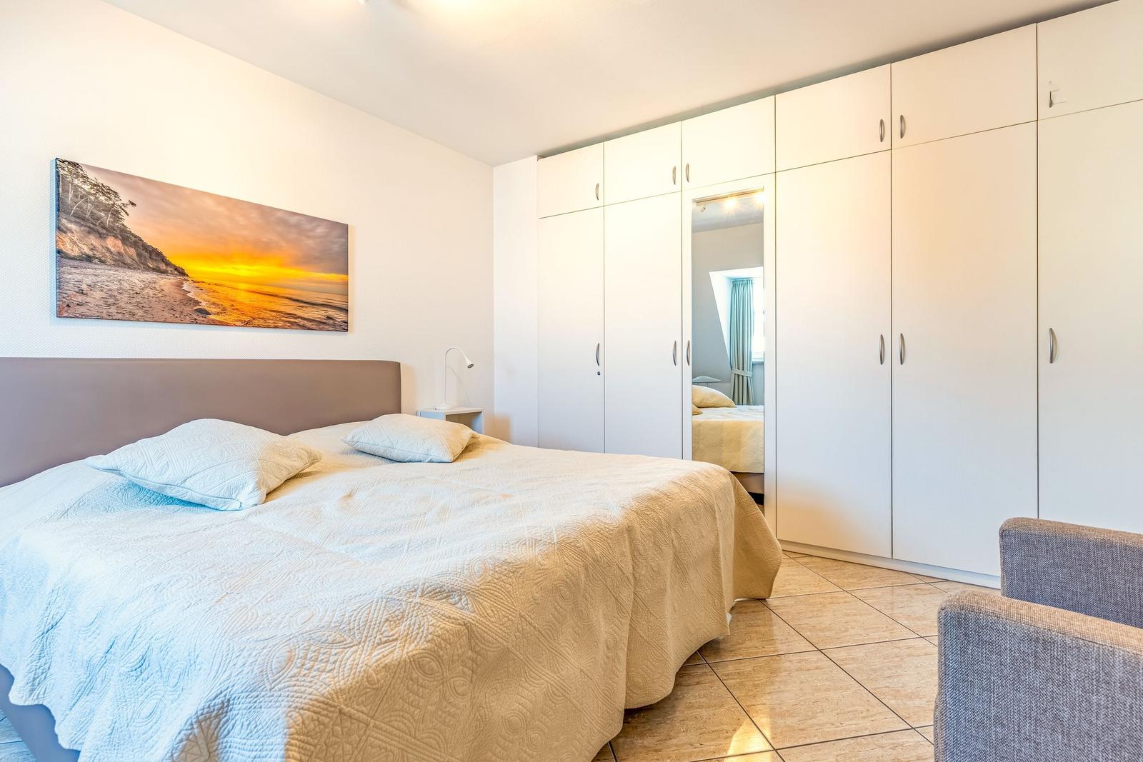 Schlafzimmer mit Doppelbett, Kleiderschrank und Wandbild.