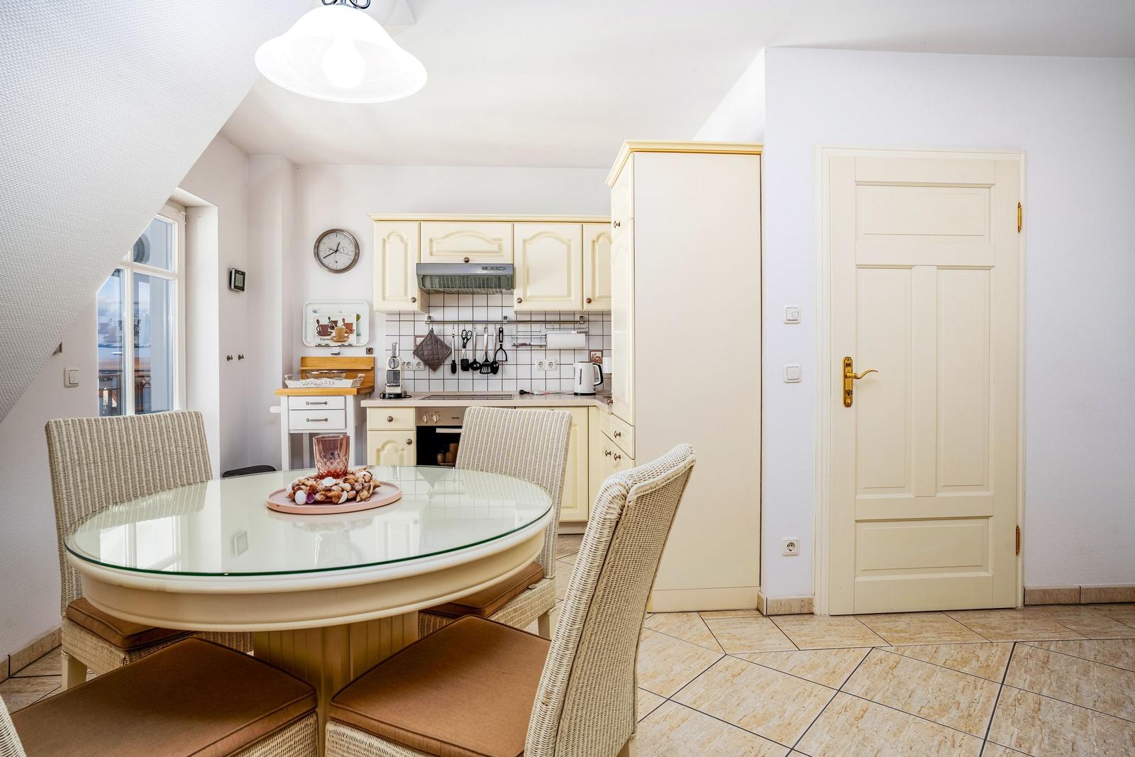 Esszimmer mit runden Tisch und Stühlen, Küche mit weißen Schränken und Fenster