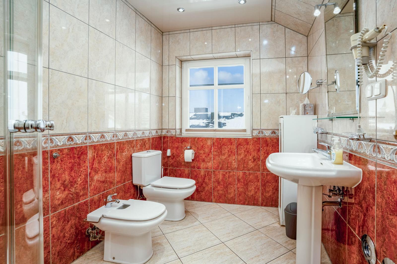 Badezimmer mit Toilette, Bidet, Waschbecken und Dusche. Rote und beige Fliesen.