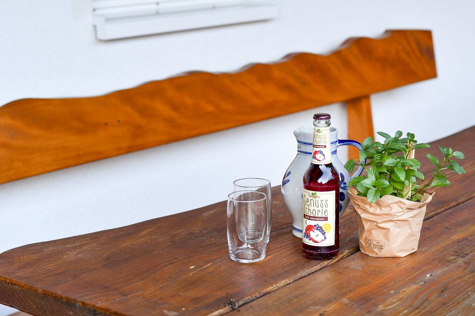 Holztisch mit Flasche, Gläsern und Pflanze im Freien.