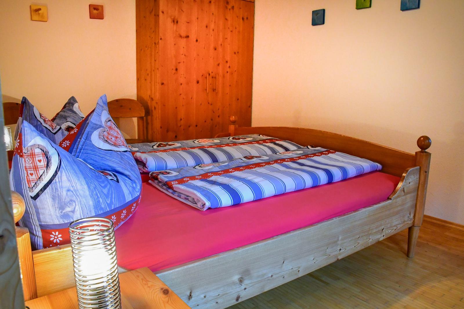 Ein Bett mit Holzrahmen, roter Matratzenauflage und blau-weiß gestreifter Bettwäsche.