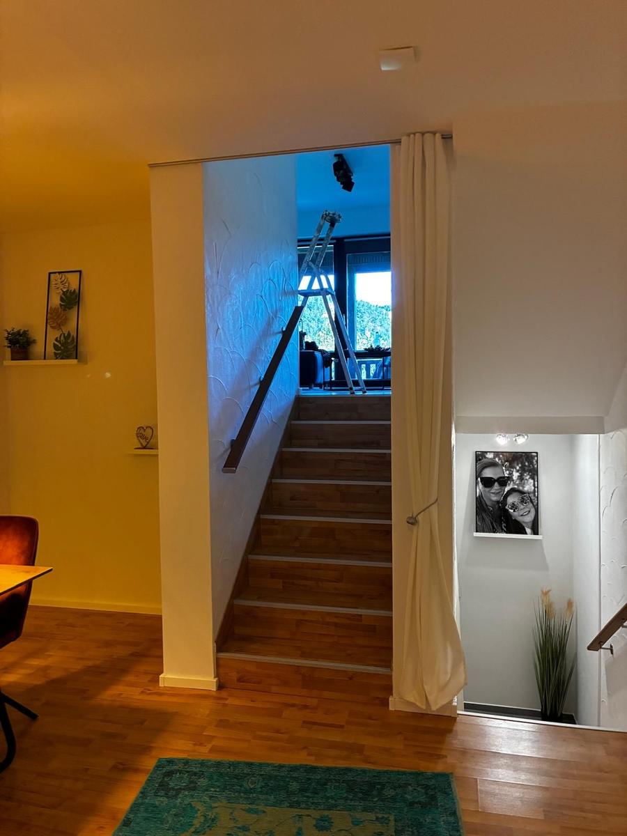 Treppenhaus mit Holztreppe und Vorhang. Im Hintergrund ist ein Ladder und ein Fenster sichtbar.