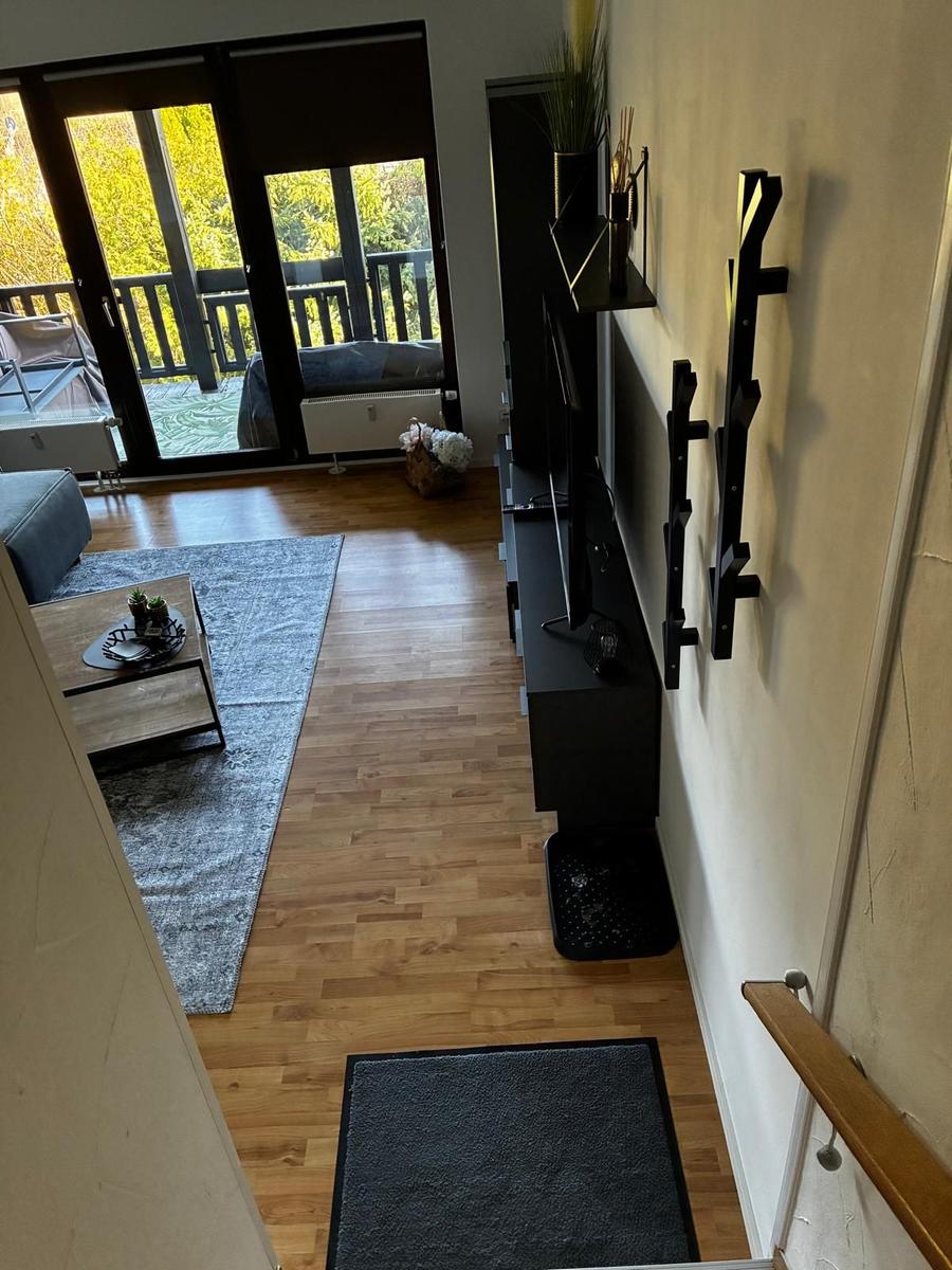 Wohnzimmer mit Holzboden, TV und Balkonzugang.