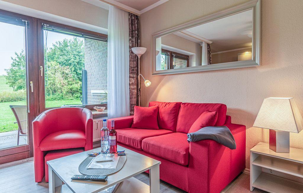 Ein Wohnzimmer mit rotem Sofa und Sessel, Tisch und Spiegel an der Wand.