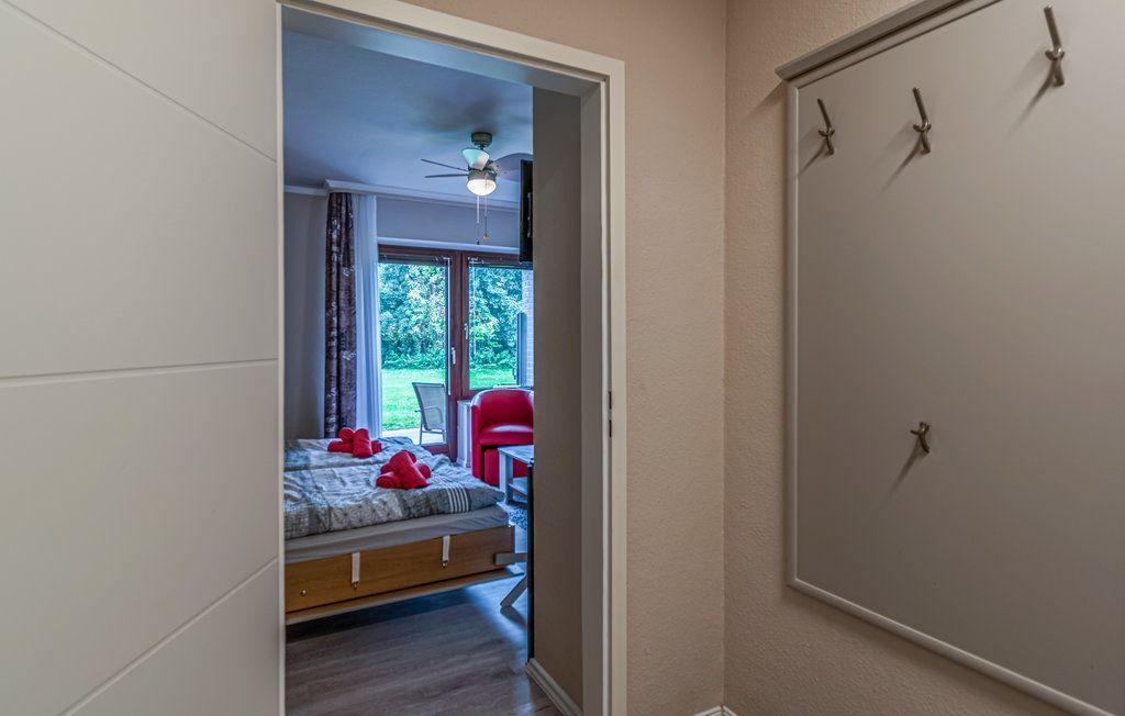 Schlafzimmer mit Bett, rotem Sessel und Blick auf Garten. Flur mit Garderobenwand.