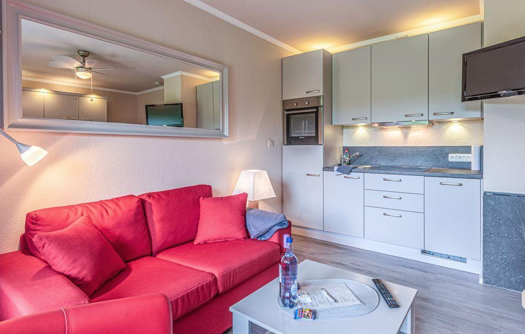 Ein Wohnbereich mit rotem Sofa, Küchenzeile und Spiegel an der Wand.