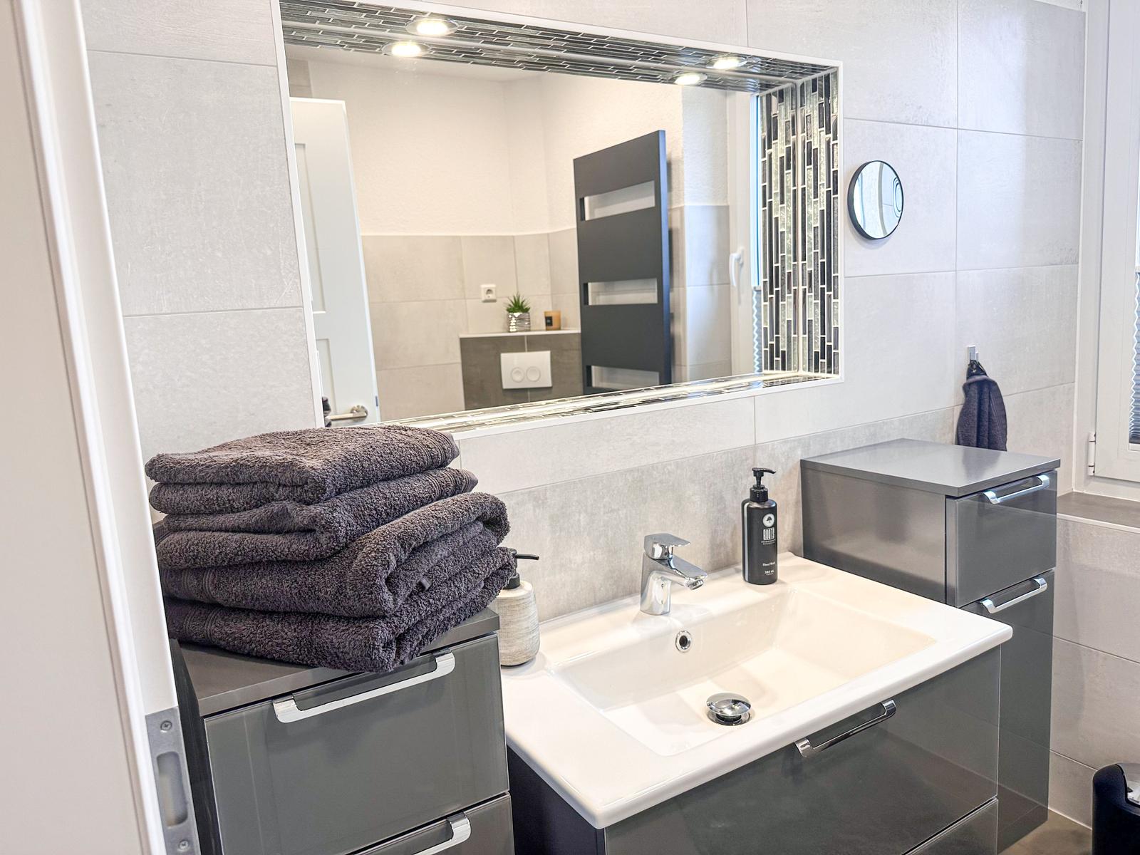 Badezimmer mit Waschbecken, Spiegel und Handtüchern.