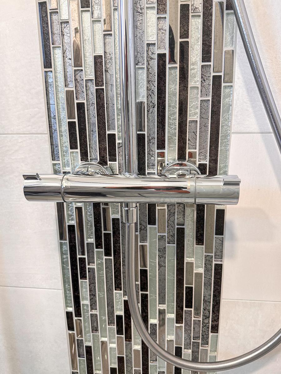 Duschbereich mit chromfarbenem Wasserhahn und Glasmosaikwand