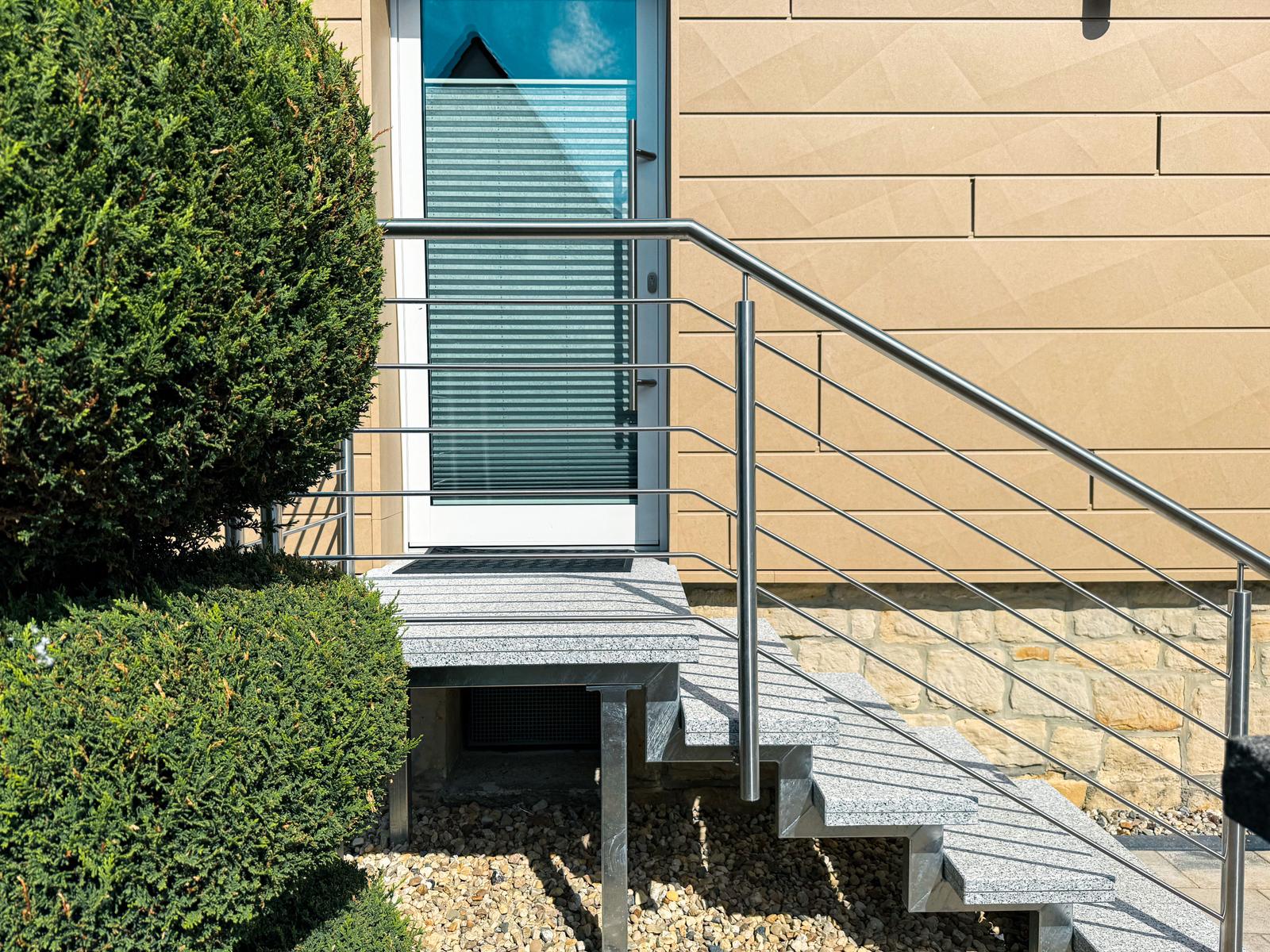 Eingangstreppe mit Metallgeländer und Steinplatten führt zur Haustür.