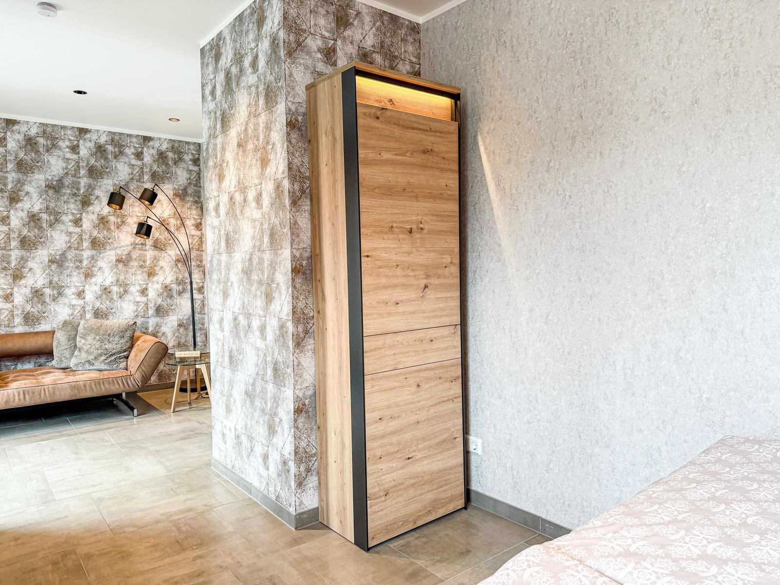 Schlafzimmer mit Bett, Kleiderschrank und Sofa im Hintergrund.