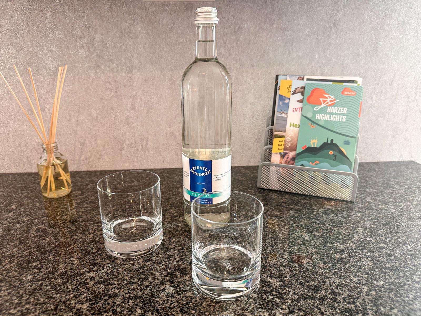 Auf der Arbeitsfläche stehen eine Flasche Mineralwasser, zwei Gläser und ein Duftspender.