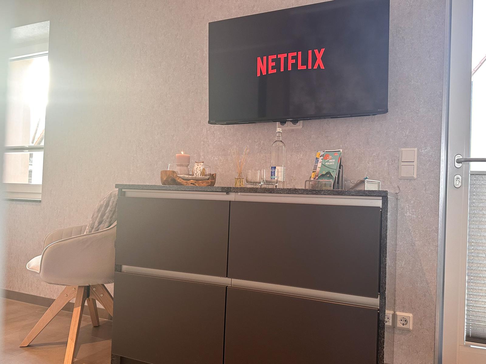 TV an der Wand, Barhocker und Getränke auf einem Schrank.