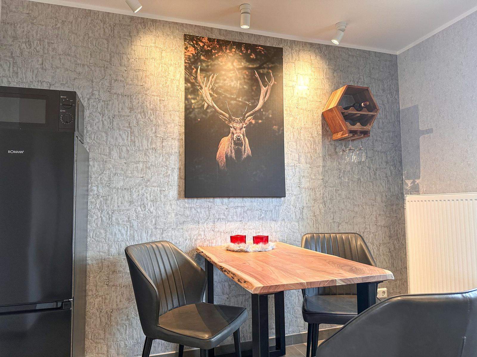 Essbereich mit Holztisch, schwarzen Stühlen und Wandbild eines Hirsches.