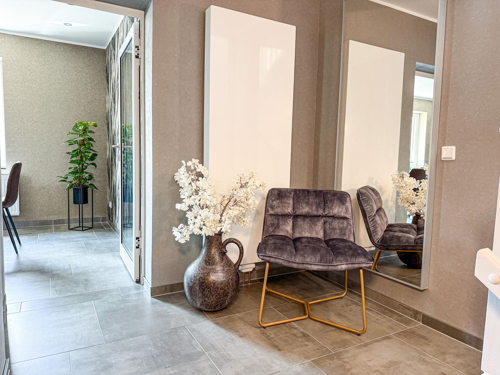 Eingangsbereich mit Sitzgelegenheit, Spiegel und Vasen mit weißen Blumen.