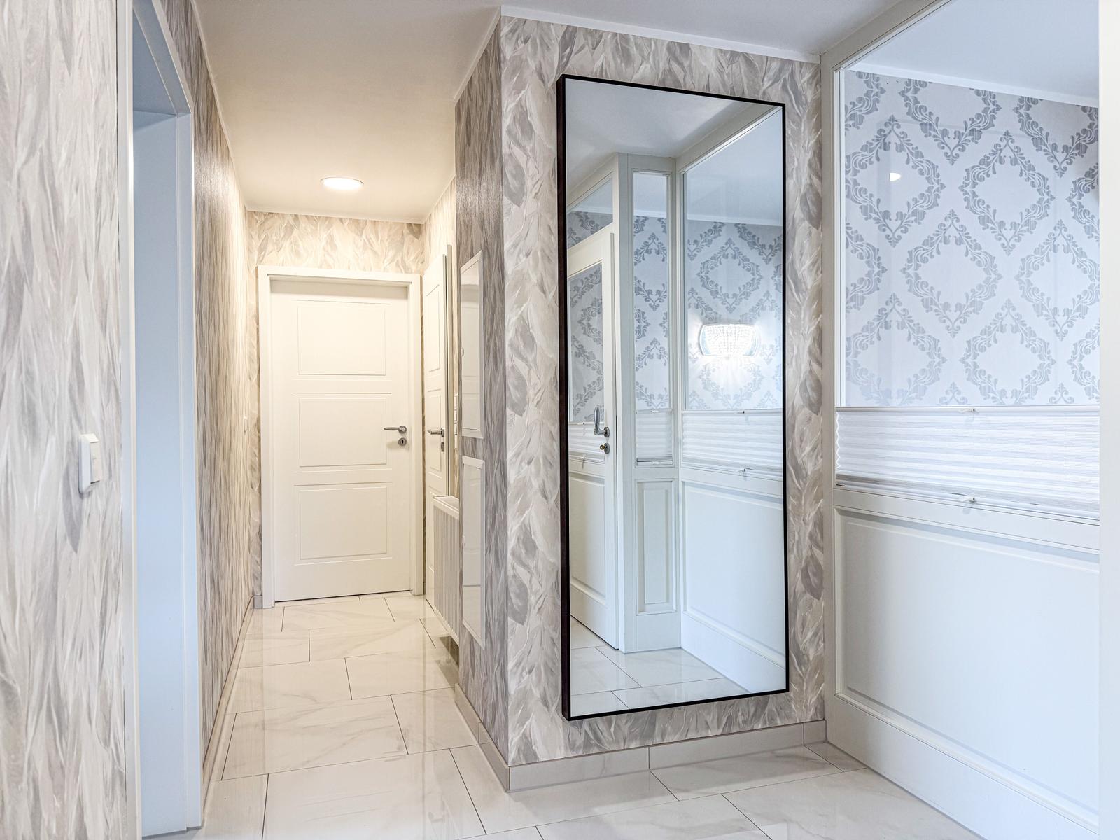 Flur mit Spiegel, Fenster und weißen Türen. Marmorierte Wände und Bodenfliesen.