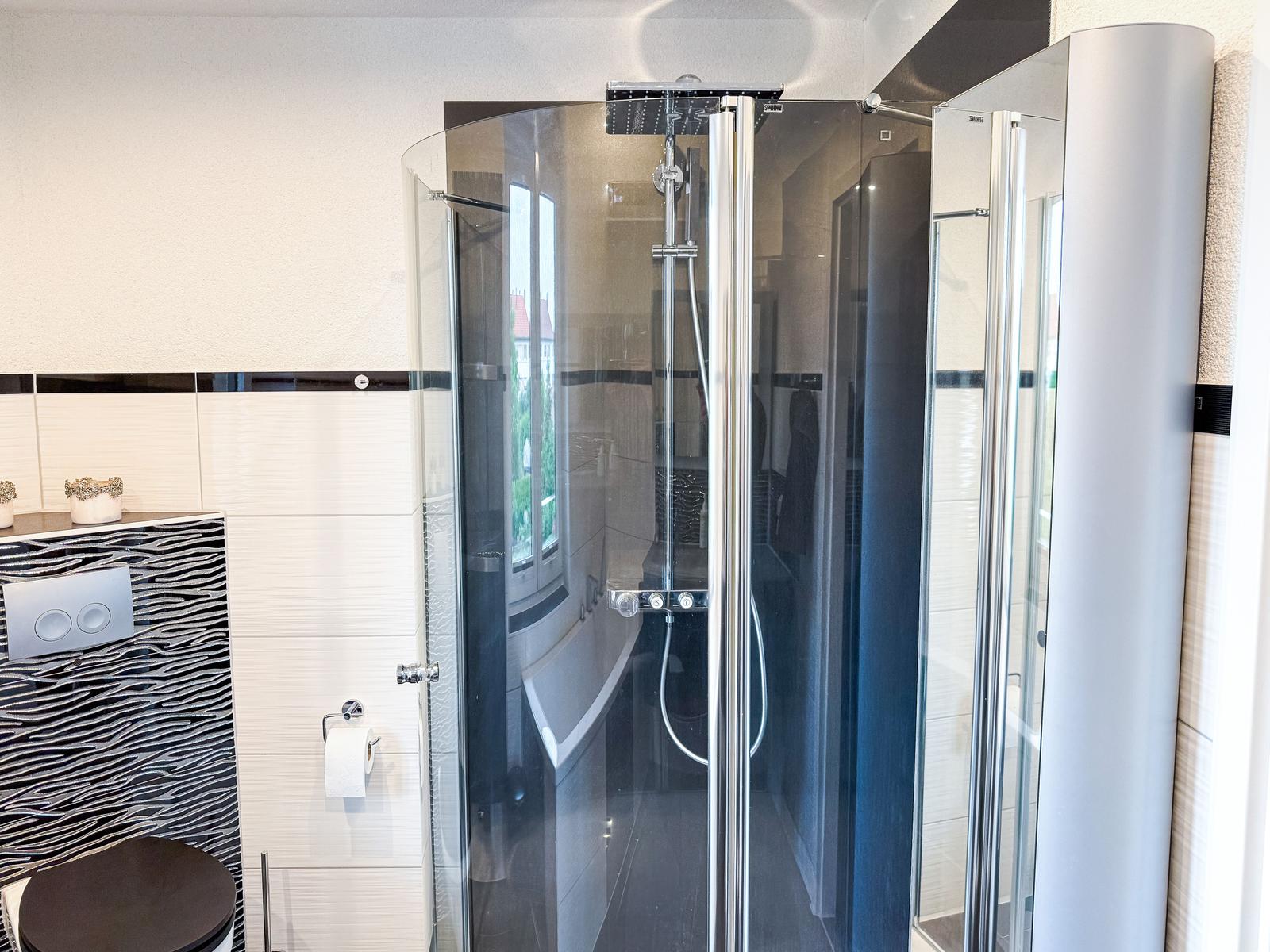 Duschkabine mit Glaswand und Duschbrause. Toilette und WC mit Wandhalterung.