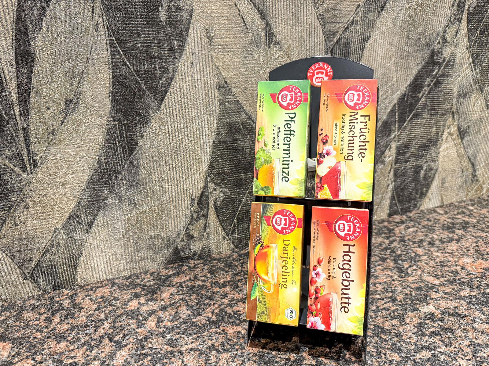 Vier Teeboxen auf einem schwarzen Halter auf Marmoroberfläche.