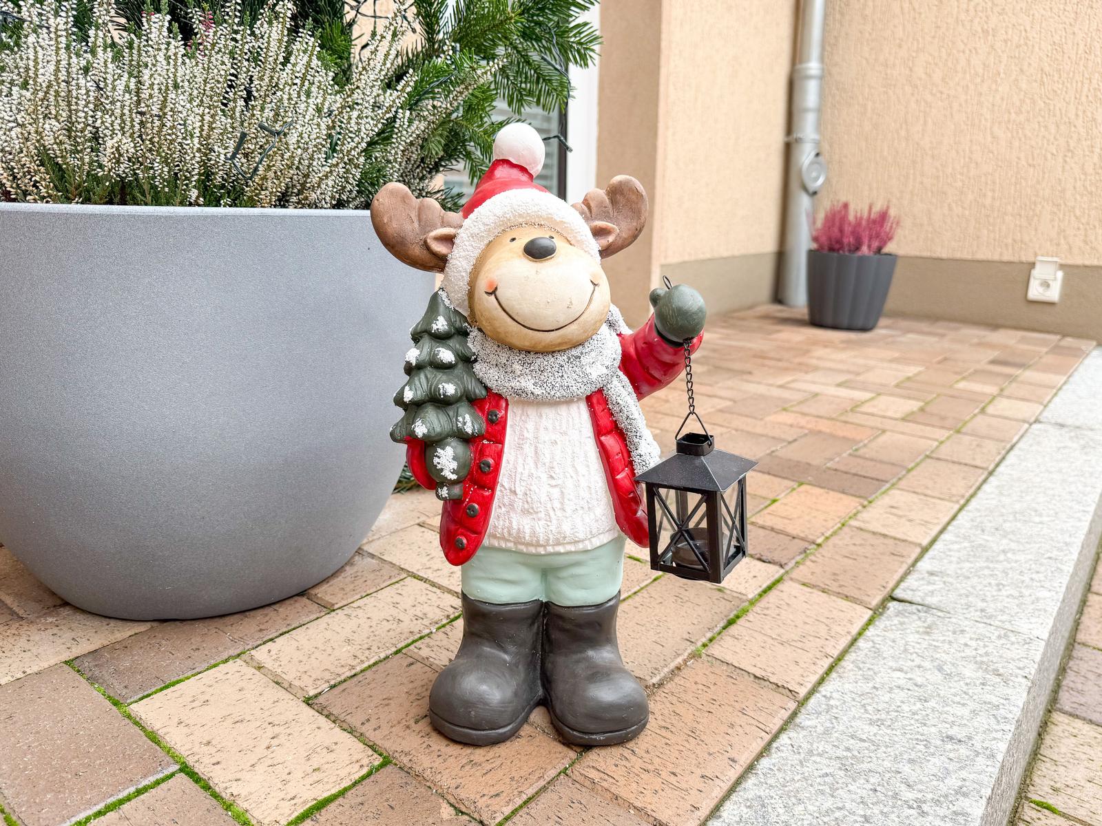 Weihnachtsreindeer mit Laterne und Tannenbaum auf Terrasse neben Pflanzen