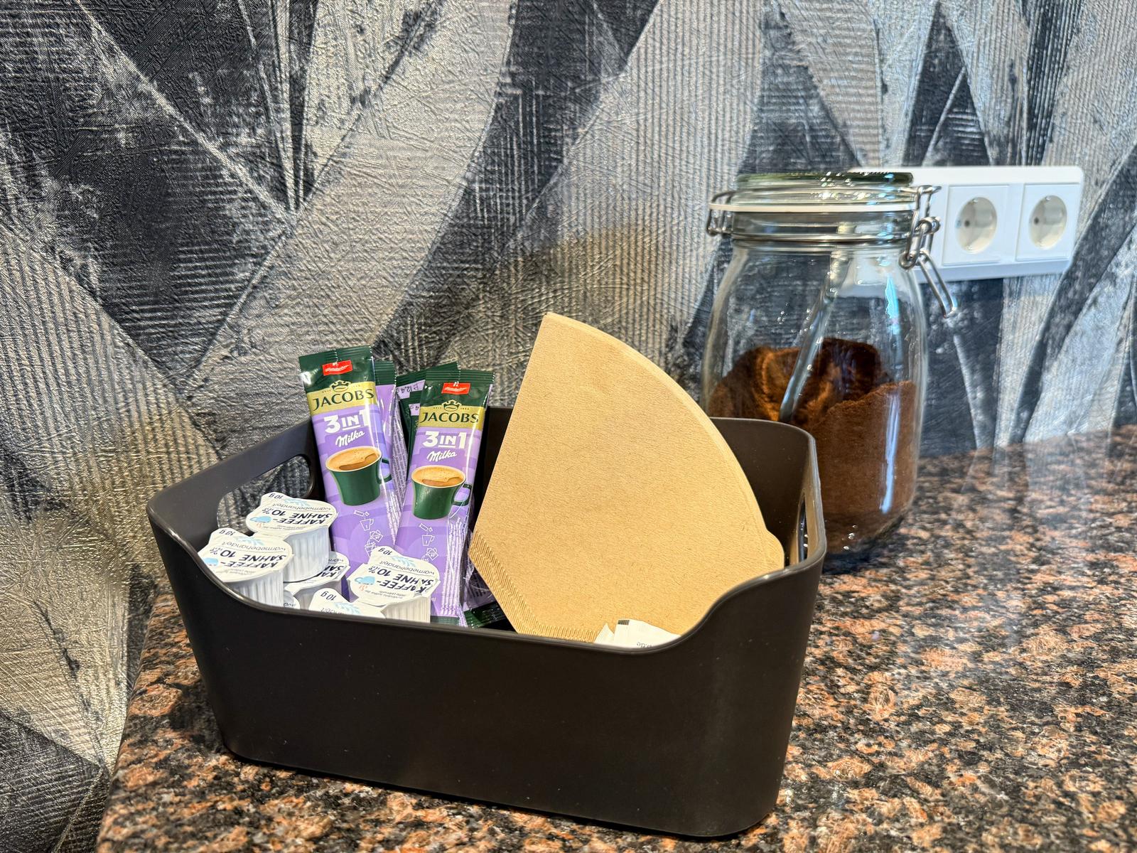 Kaffee- und Zuckertütchen in einem Behälter auf der Arbeitsfläche.