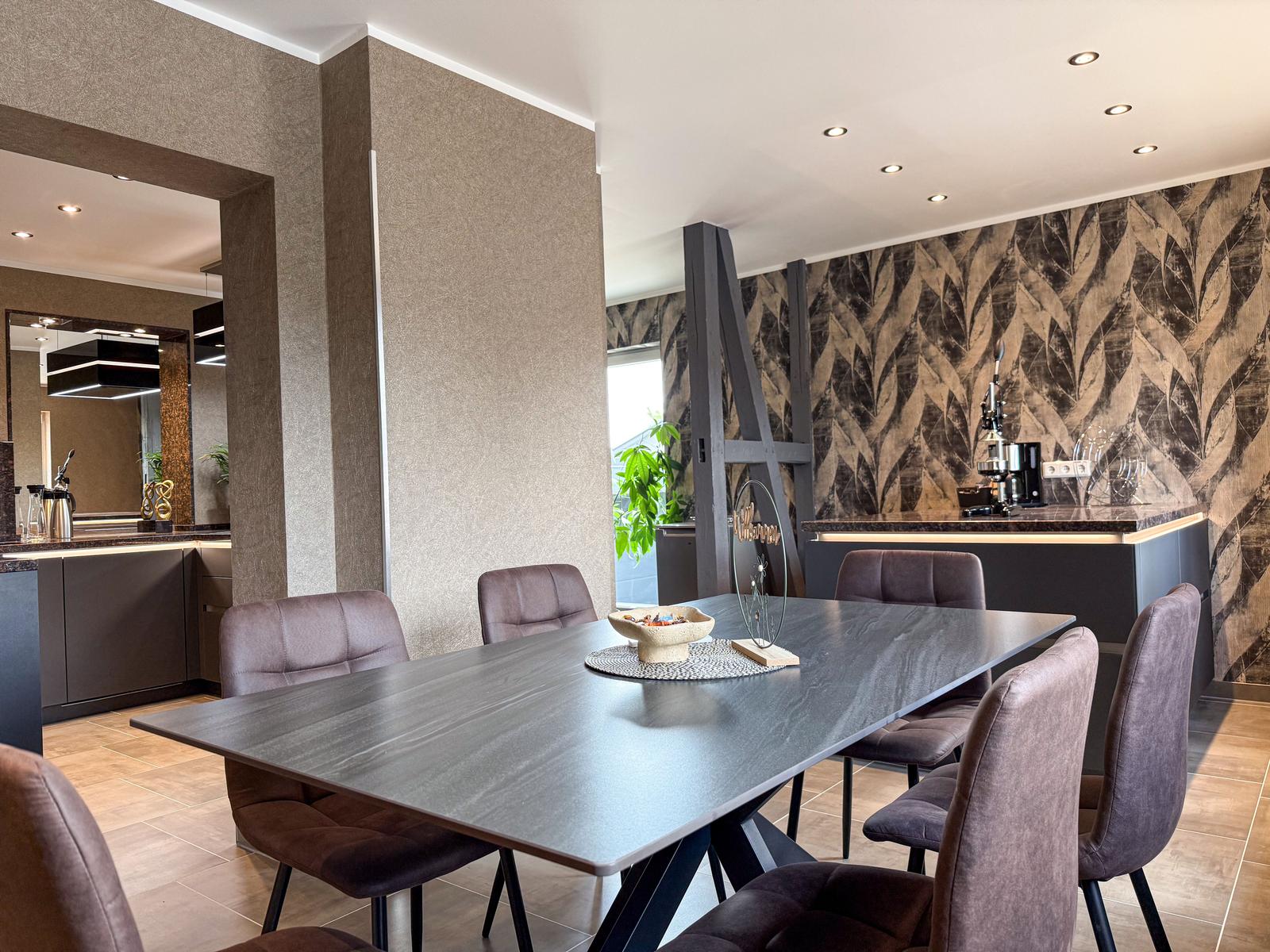 Esszimmer mit dunklem Tisch, Stühlen und Wandtapete mit Blattmuster.