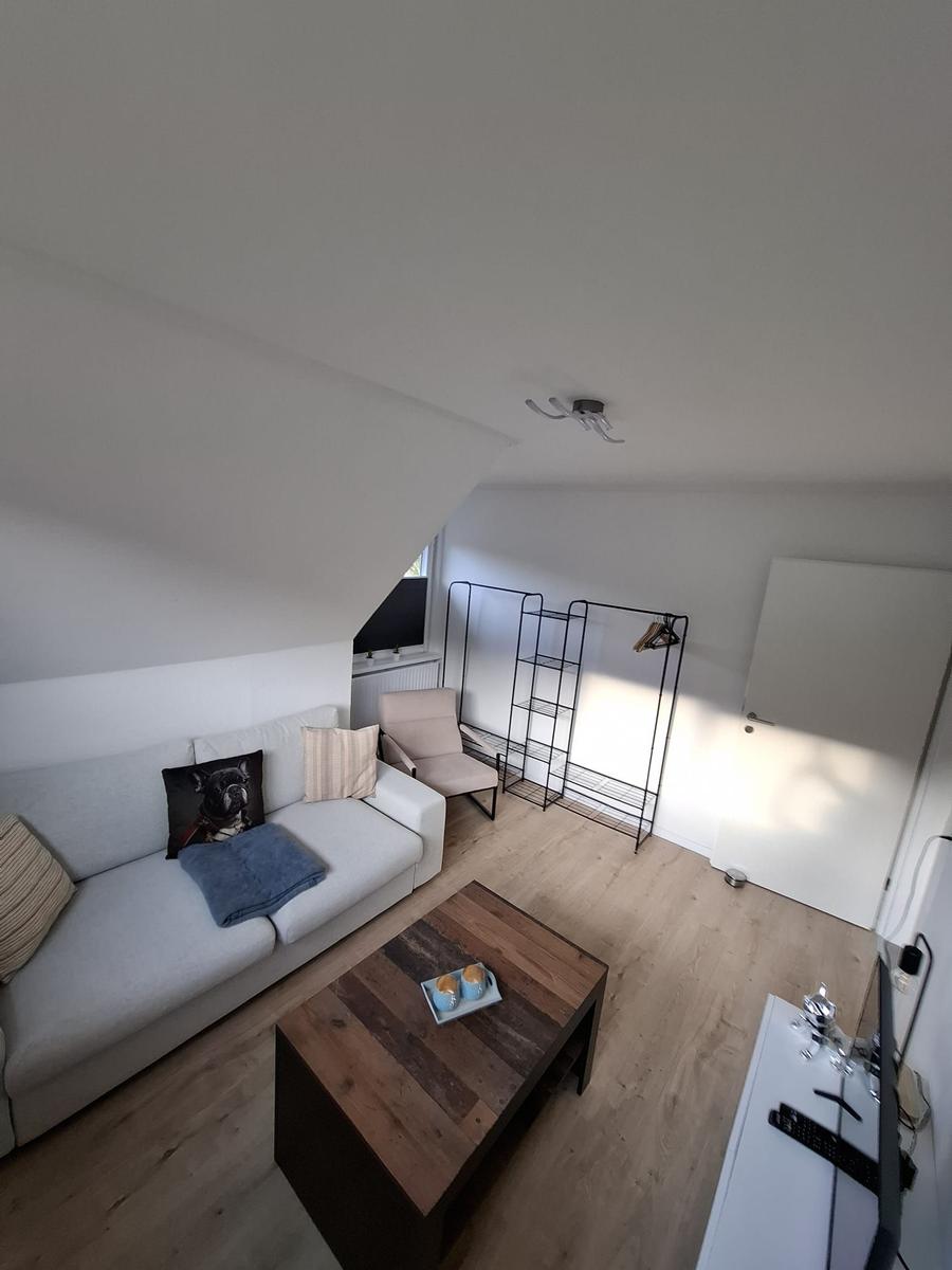 Wohnzimmer mit Sofa, Couchtisch und Kleiderständer unter schrägem Dach