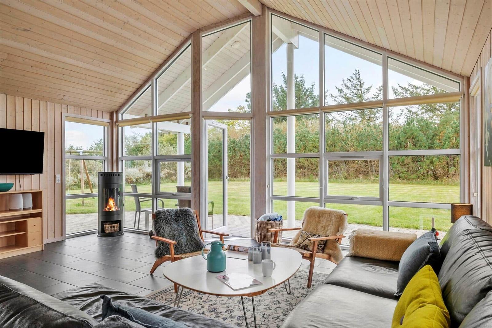 Living room with fireplace, seating, and large windows overlooking green areas.