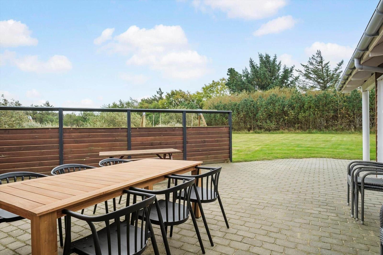 Terrace with table and chairs, lawn and forest in the background.